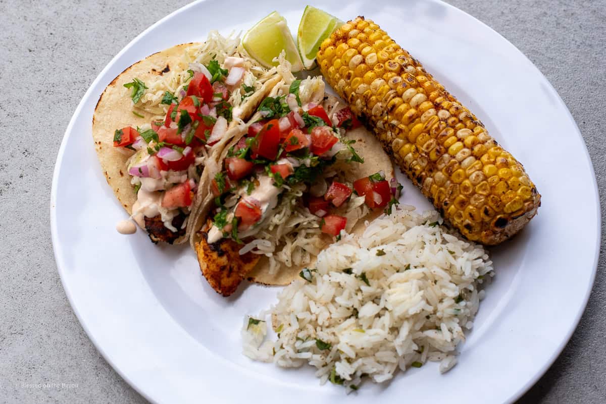 Fish Tacos on a white place with grilled sweet corn and cilantro lime rice