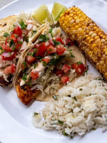 Fish Tacos on a white place with grilled sweet corn and cilantro lime rice