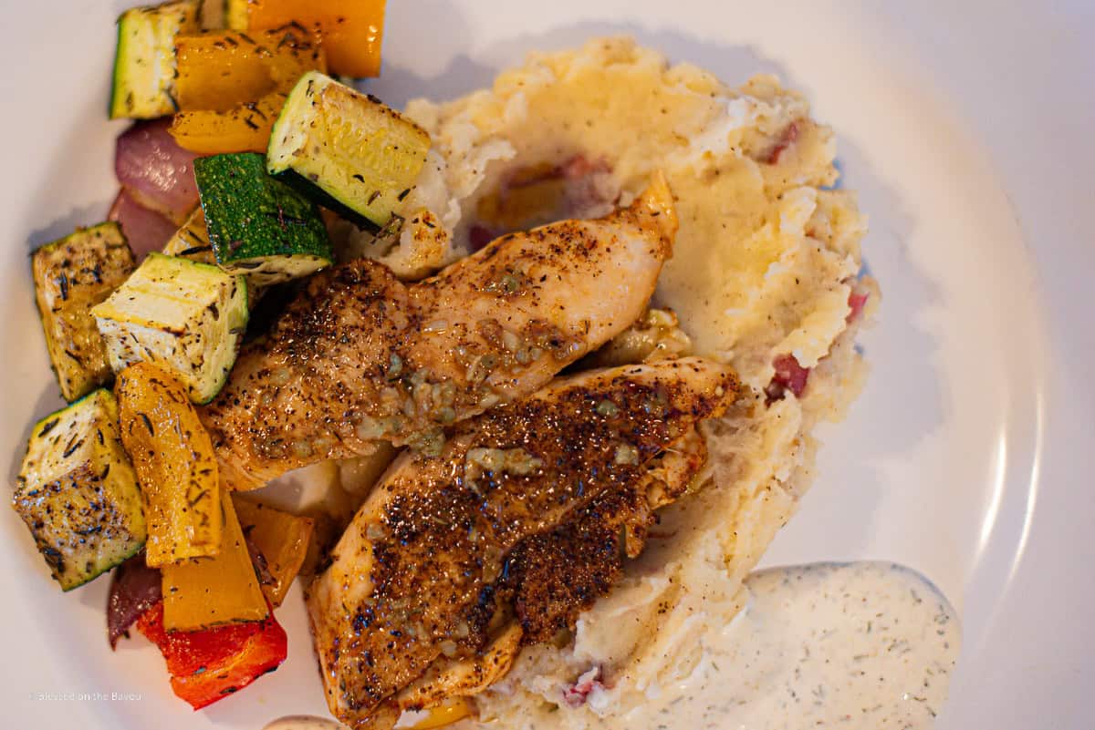 Lemon Garlic Chicken Plated on top of mashed potatoes with roasted veggies and creamy herb sauce