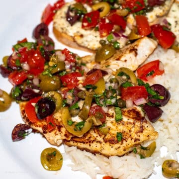 Red Snapper on a white plate with olives tomatoes capers onions