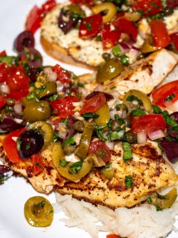Red Snapper on a white plate with olives tomatoes capers onions