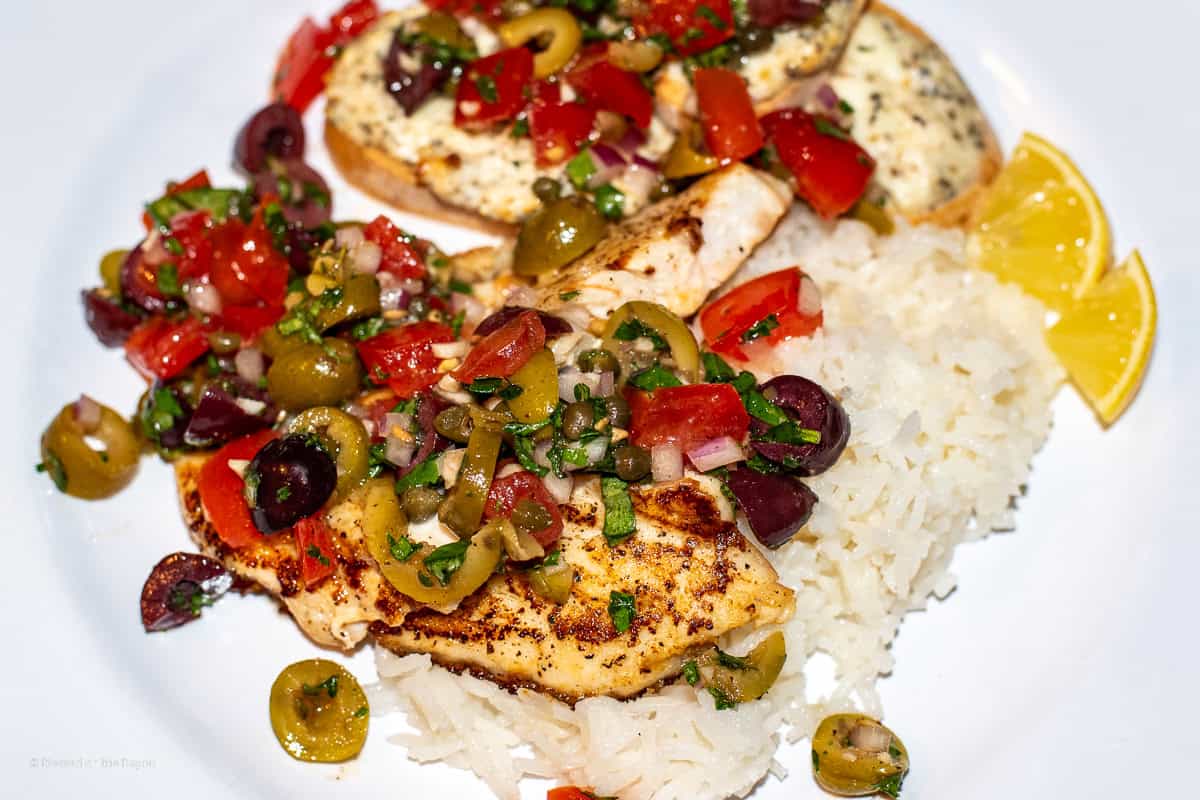 Red Snapper on a white plate with olives tomatoes capers onions