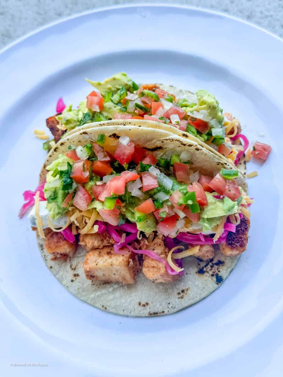 Cajun white fish tacos topped with avocado, pico de gallo, pickled red cabbage, and lime-jalapeño sauce